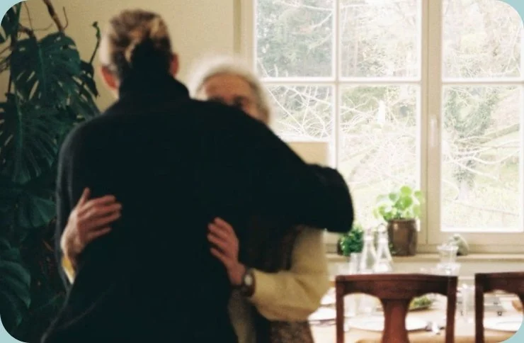 Two people hugging in a sunlit dining room
